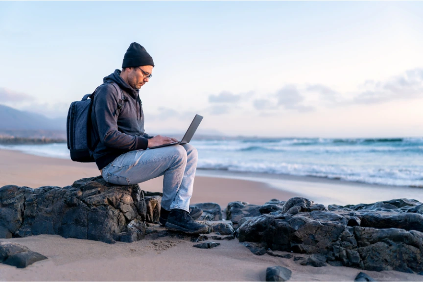 A person working on a laptop while travelling, with a view of a beach